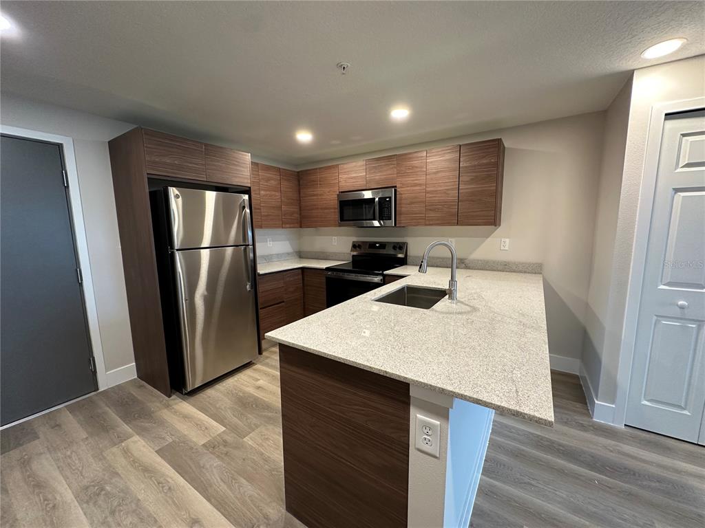 A kitchen features wood-grain cabinets, stainless steel appliances, and a granite-topped island with a sink — 4424 S TEXAS AVENUE UNIT 110, ORLANDO, FL