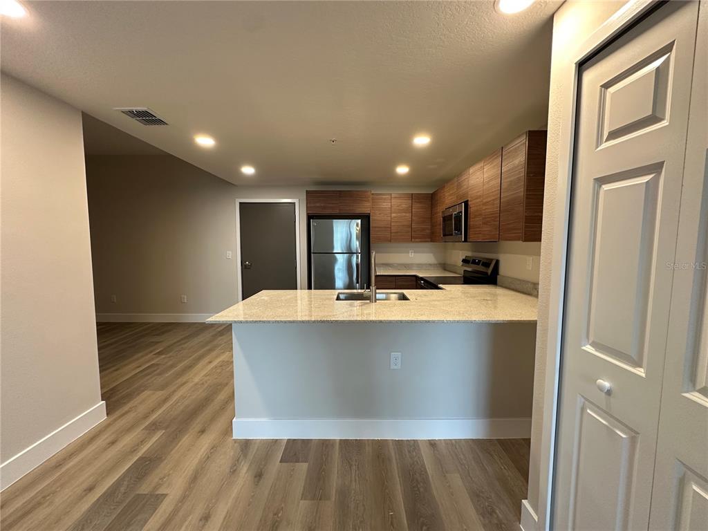 A kitchen with wood-toned cabinets, granite countertops, and light wood-look flooring — 4424 S TEXAS AVENUE UNIT 110, ORLANDO, FL