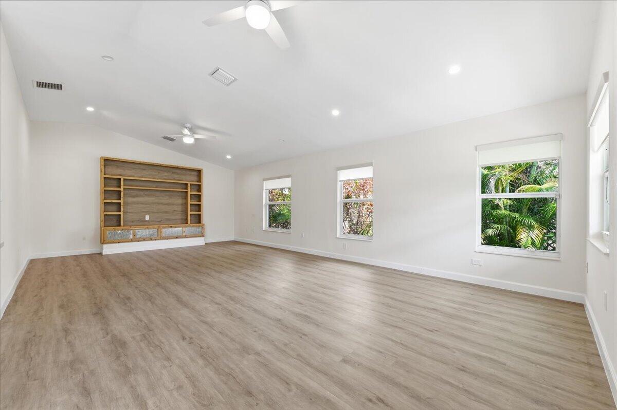 A spacious living room features light wood-look flooring, white walls, and a built-in wooden entertainment center — 530 NE 3rd Avenue NE, Delray Beach FL 33444, DELRAY BEACH, FL