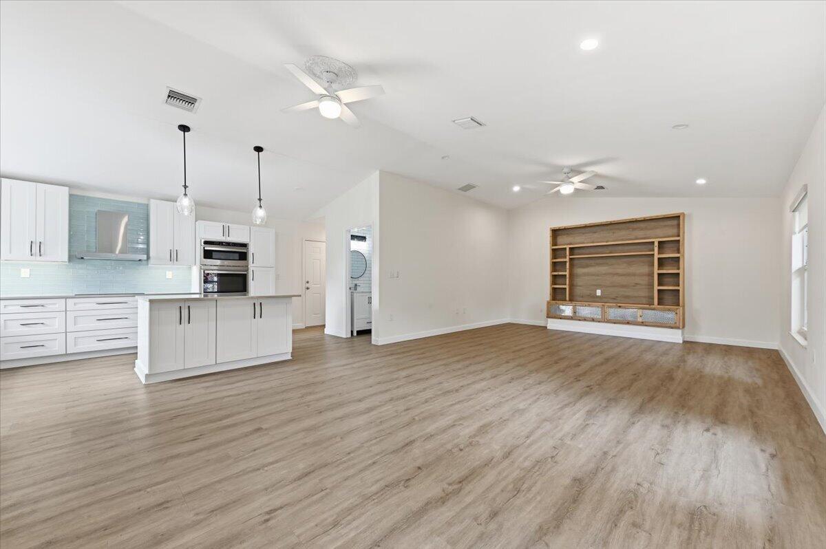 An open-concept kitchen and living area features white cabinetry, wood-look flooring, and a built-in entertainment center — 530 NE 3rd Avenue NE, Delray Beach FL 33444, DELRAY BEACH, FL