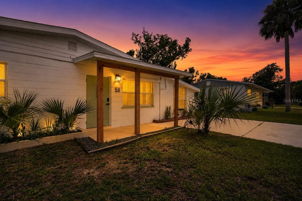 A white single-story house with a wooden porch and palm trees at sunset — 94 ROGERS PARK DRIVE, ORMOND BEACH, FL