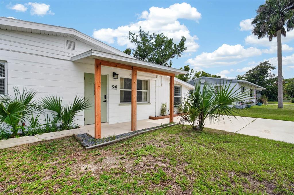 A white single-story house with a wooden-post porch and a green front door — 94 ROGERS PARK DRIVE, ORMOND BEACH, FL