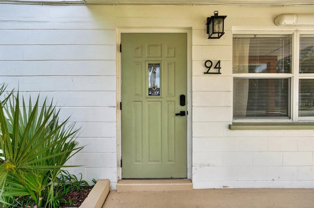 A sage green front door with a small window is set in a white wall — 94 ROGERS PARK DRIVE, ORMOND BEACH, FL