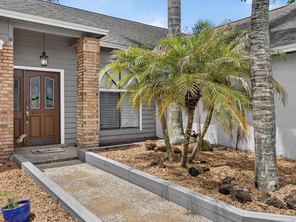 A gray house exterior features a brown front door, brick columns, and a palm tree — 4609 TIFFANY WOODS CIRCLE, OVIEDO, FL