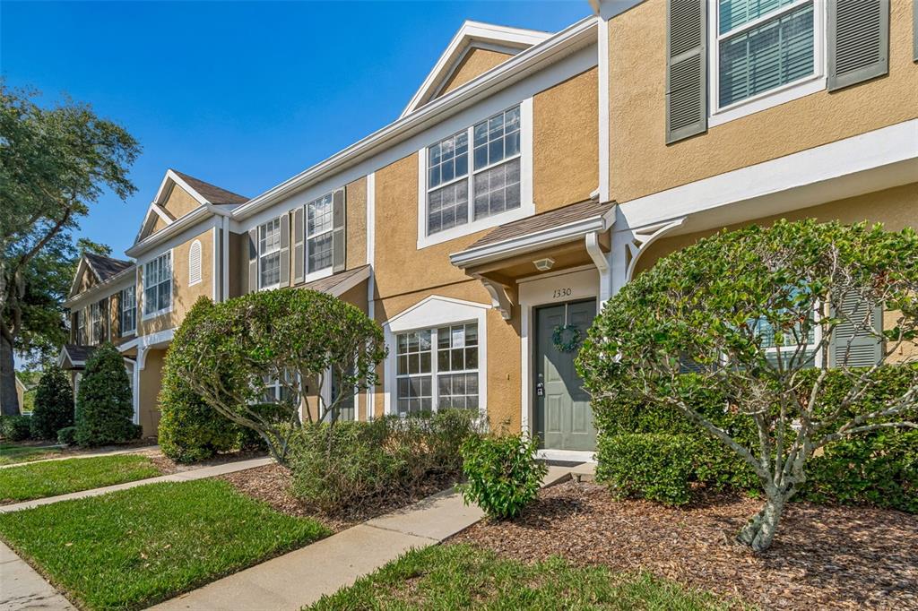 A two-story tan townhouse with a green front door and a landscaped front yard — 1330 STANDRIDGE DRIVE, WESLEY CHAPEL, FL