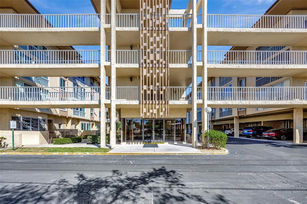 A multi-story apartment building exterior features a central glass entrance and open-air balconies — 113 ISLAND WAY UNIT 241, CLEARWATER BEACH, FL