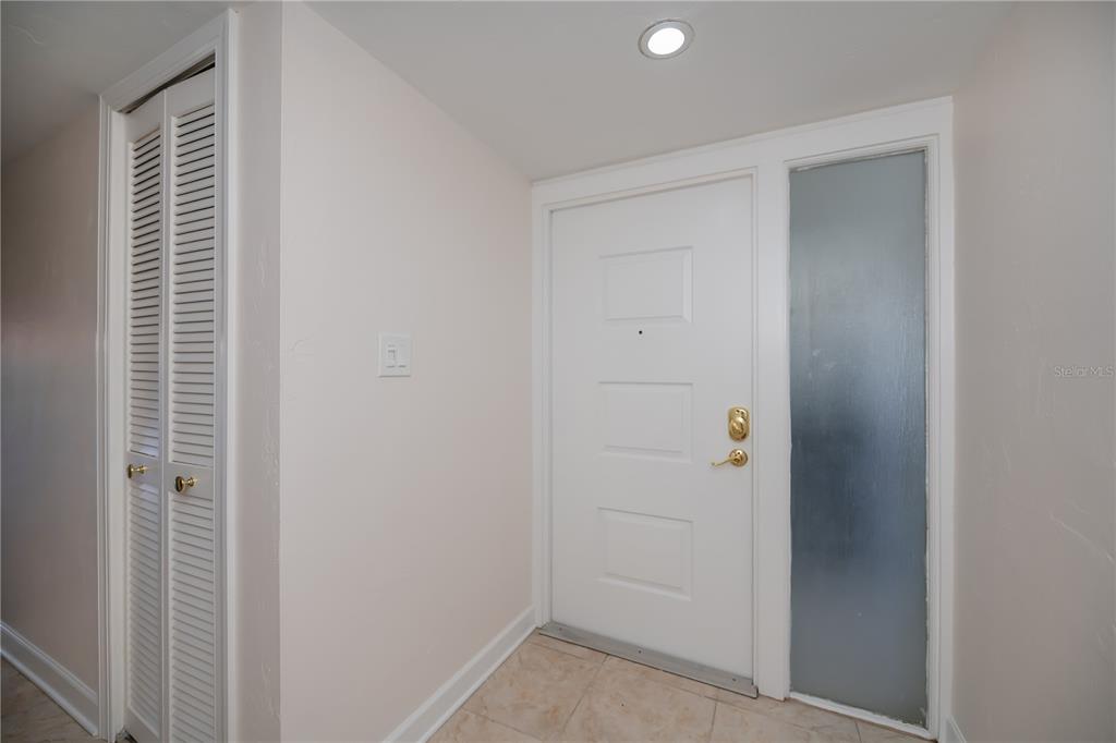 An entryway features a white front door with a sidelight, tiled flooring, and louvered closet doors — 4396 BOWSPRIT COURT UNIT 4E, FORT MYERS, FL