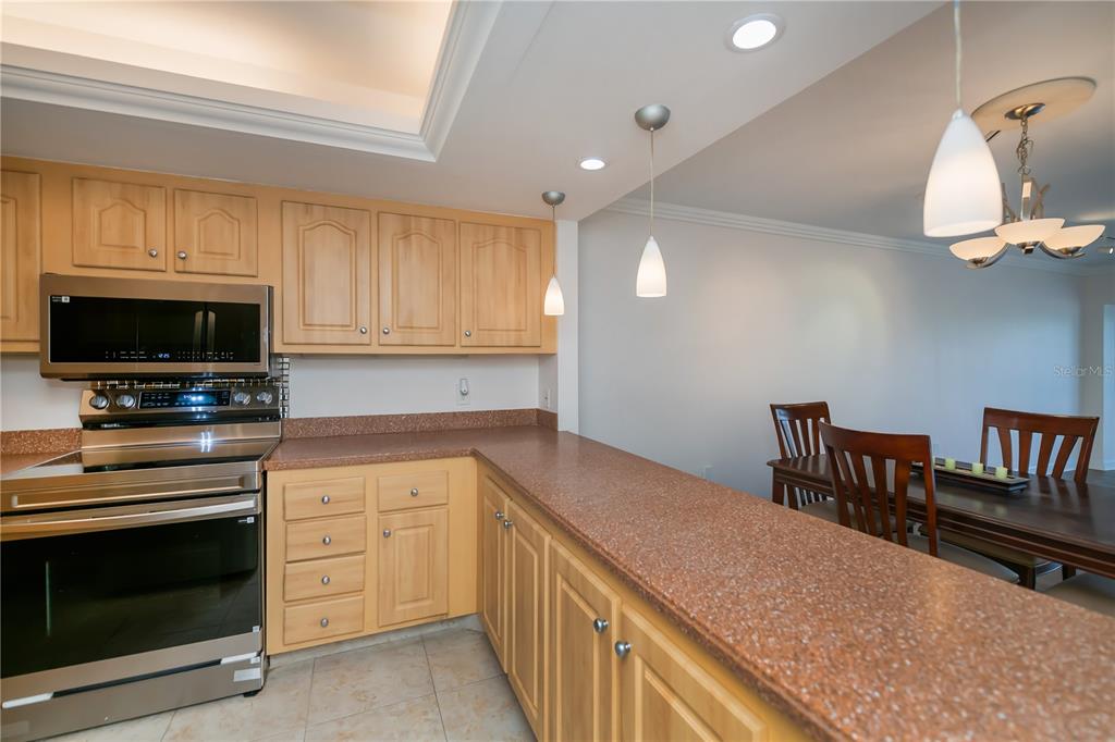 A kitchen with light wood cabinets, granite countertops, and stainless steel appliances overlooks a dining area — 4396 BOWSPRIT COURT UNIT 4E, FORT MYERS, FL