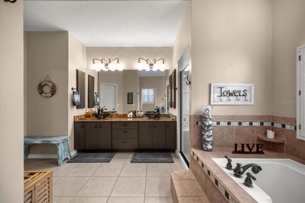 A bathroom features a double vanity with dark cabinets, a soaking tub, and tiled floors — 4860 W ANGUS DRIVE, BEVERLY HILLS, FL