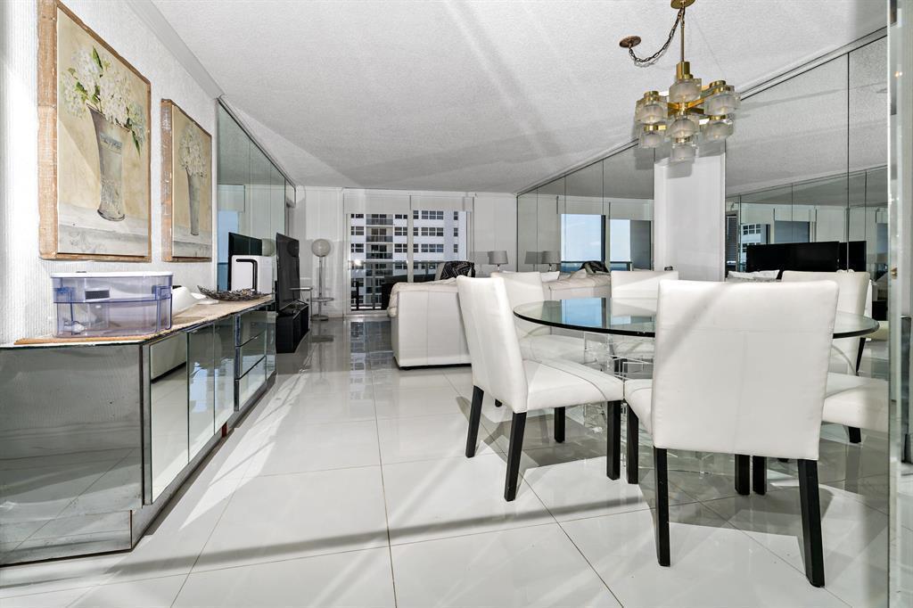 A dining area with a glass table and white chairs next to a mirrored wall — 1880 S Ocean Drive, Hallandale Beach FL 33009, HALLANDALE BEACH, FL
