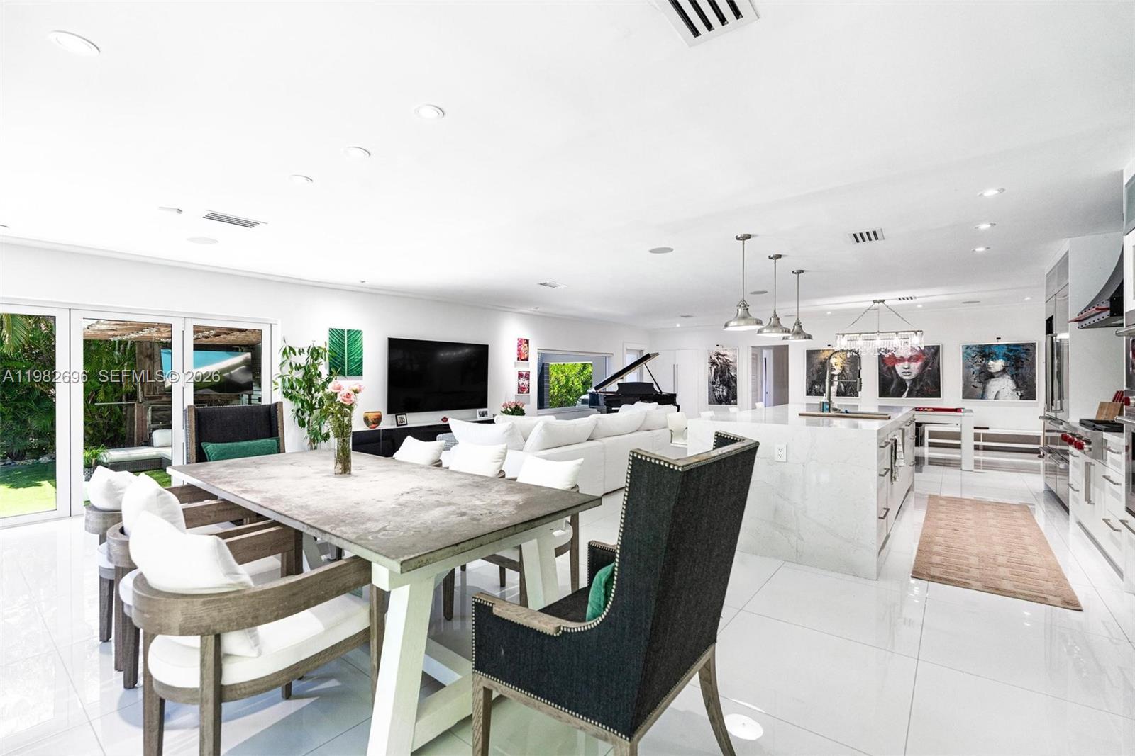A bright living room features a large white sectional sofa, a wall-mounted television, and glass doors — 1865 Daytonia Rd, Miami Beach FL 33141, MIAMI BEACH, FL
