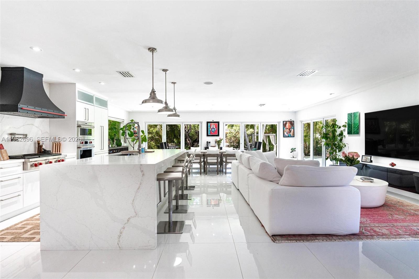 A modern open-concept kitchen and dining area features white tile floors and a large island — 1865 Daytonia Rd, Miami Beach FL 33141, MIAMI BEACH, FL
