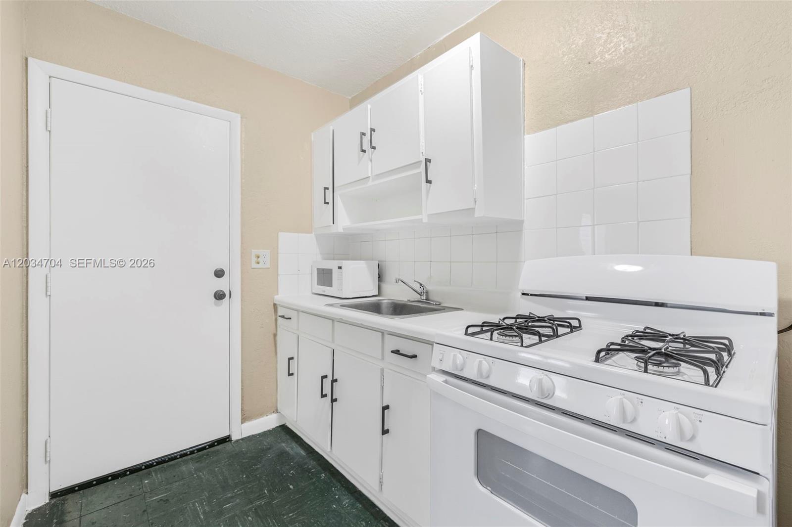 A small kitchen features white cabinets, a gas stove, a sink, and a door — 126 SW 18th Ave # 11, Miami FL 33135, MIAMI, FL