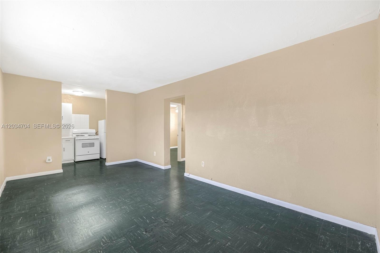 An empty room with dark green tile flooring and tan walls leads to a kitchen — 126 SW 18th Ave # 11, Miami FL 33135, MIAMI, FL