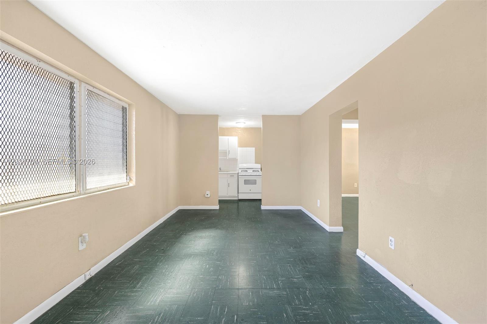 An empty room with dark green flooring leads to a small kitchen with white appliances — 126 SW 18th Ave # 11, Miami FL 33135, MIAMI, FL