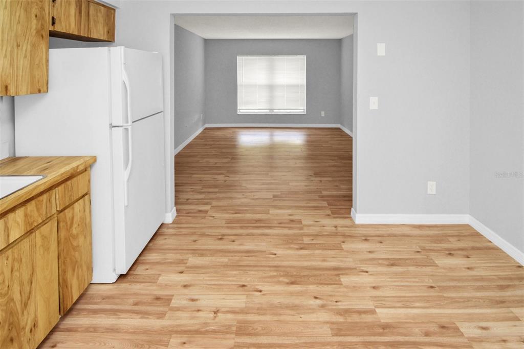 A kitchen with wood cabinets and a white refrigerator opens into a living area — 7450 35TH STREET N UNIT 1604, PINELLAS PARK, FL