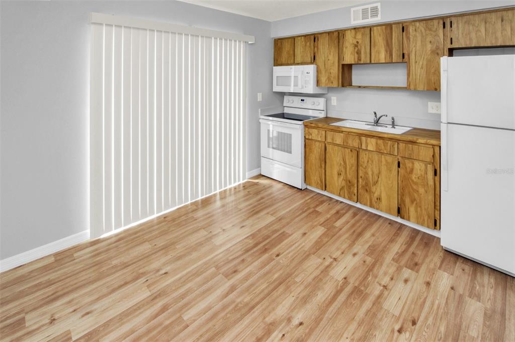 A kitchen features wood cabinets, white appliances, and light wood-look flooring next to sliding doors — 7450 35TH STREET N UNIT 1604, PINELLAS PARK, FL