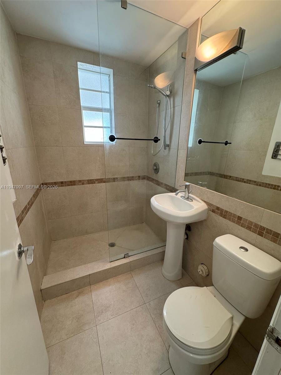 A bathroom features a glass-enclosed shower, a pedestal sink, and light-colored tile flooring — 1000 Meridian Ave # 17, Miami Beach FL 33139, MIAMI BEACH, FL