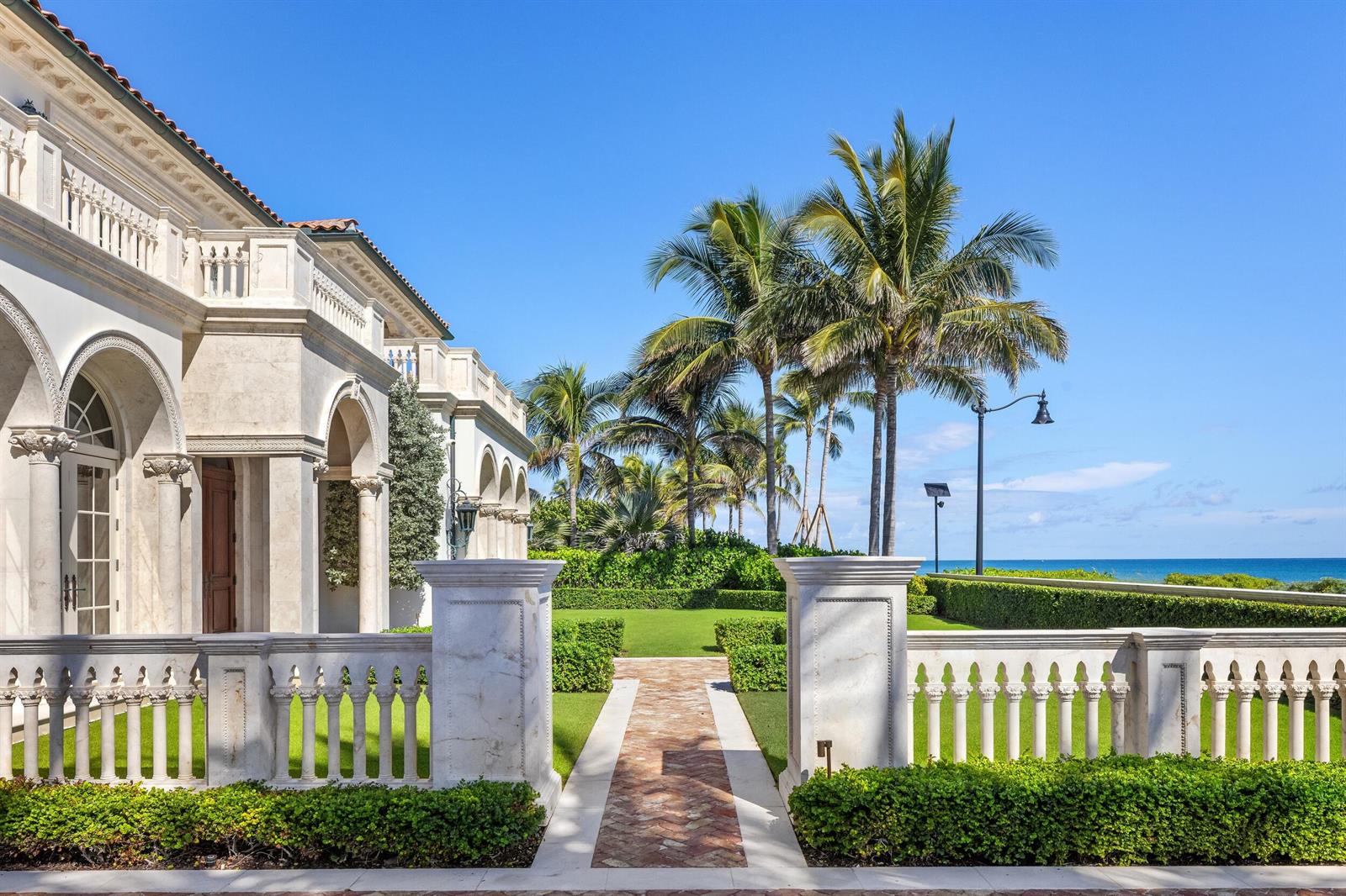 A stone balustrade and brick walkway lead toward a coastal mansion with palm trees — 1620 S Ocean Boulevard, Palm Beach FL 33480, PALM BEACH, FL
