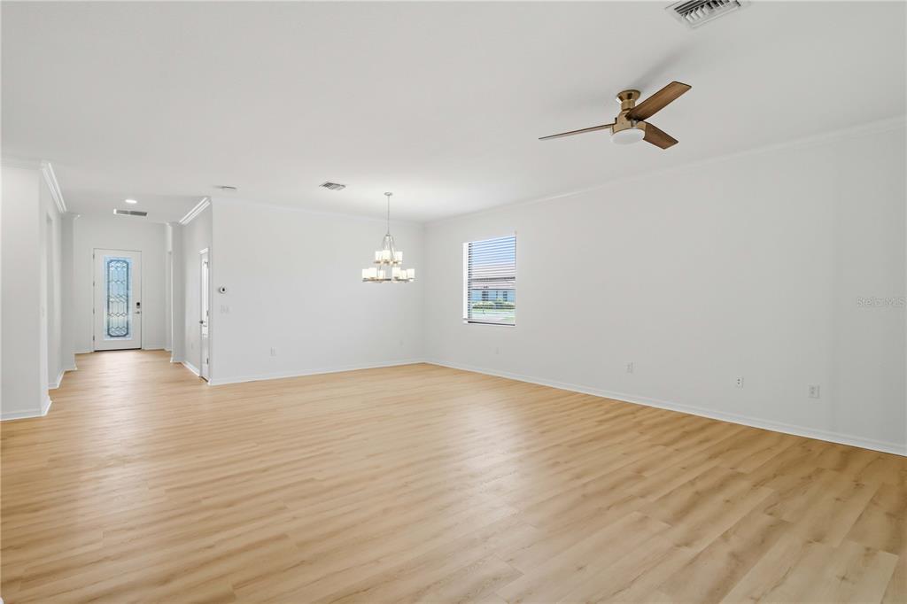 An empty living room features light wood-look flooring, white walls, a ceiling fan, and a chandelier — 19345 CRUISE DRIVE, VENICE, FL
