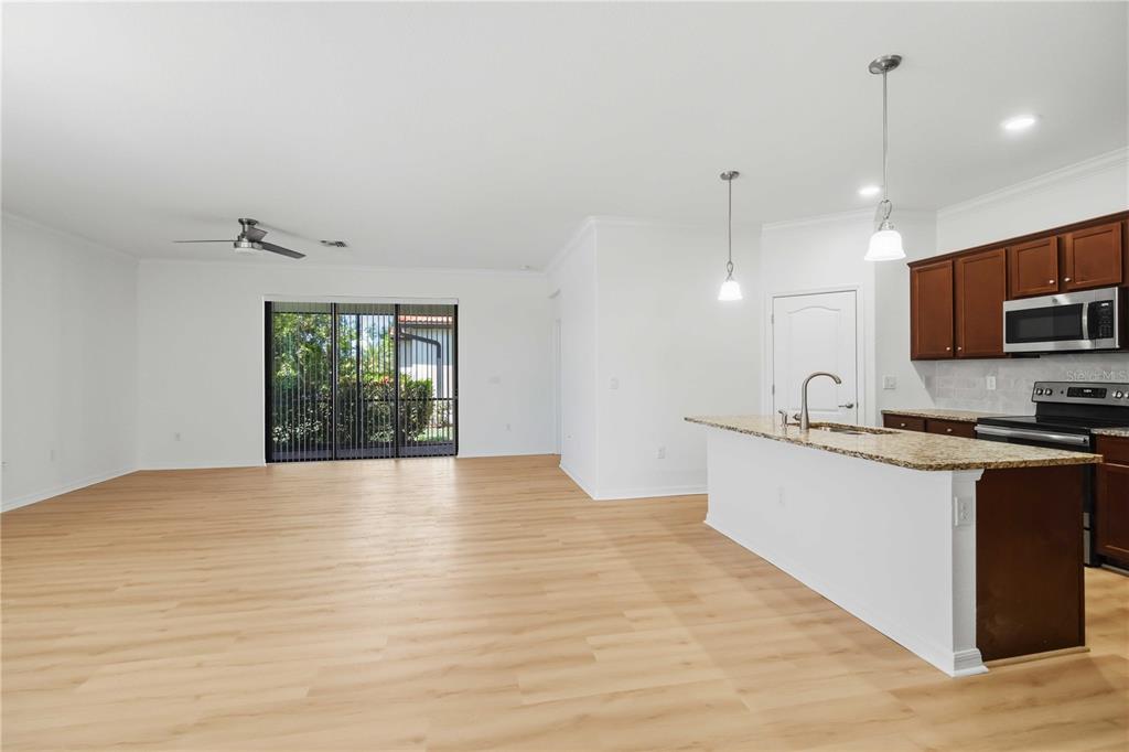 An open-concept living area with light wood flooring, a kitchen island, and sliding glass doors — 19345 CRUISE DRIVE, VENICE, FL