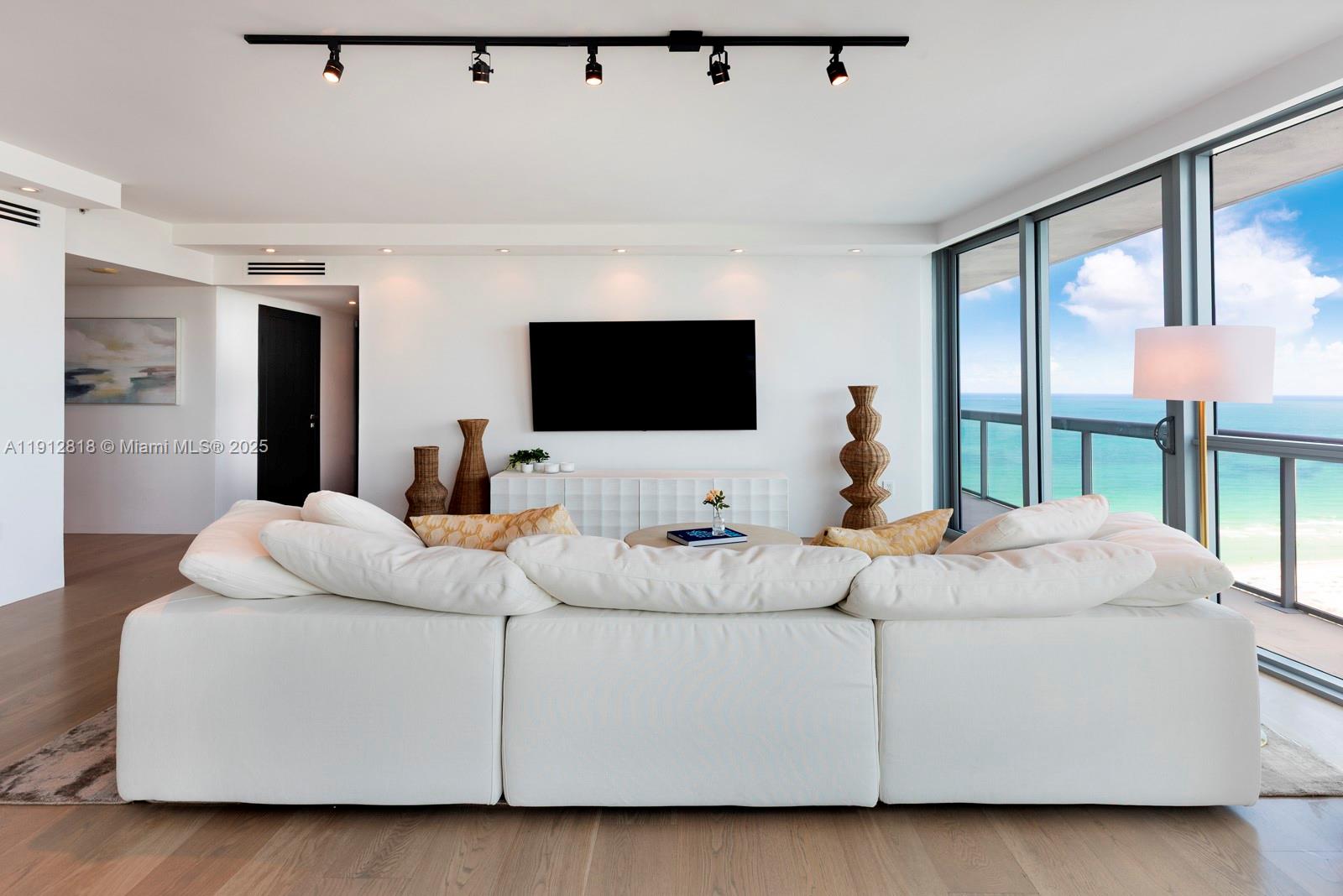 A modern living room features a white sectional sofa, wall-mounted television, and floor-to-ceiling ocean views — 101 20th St # 3006, Miami Beach FL 33139, MIAMI BEACH, FL