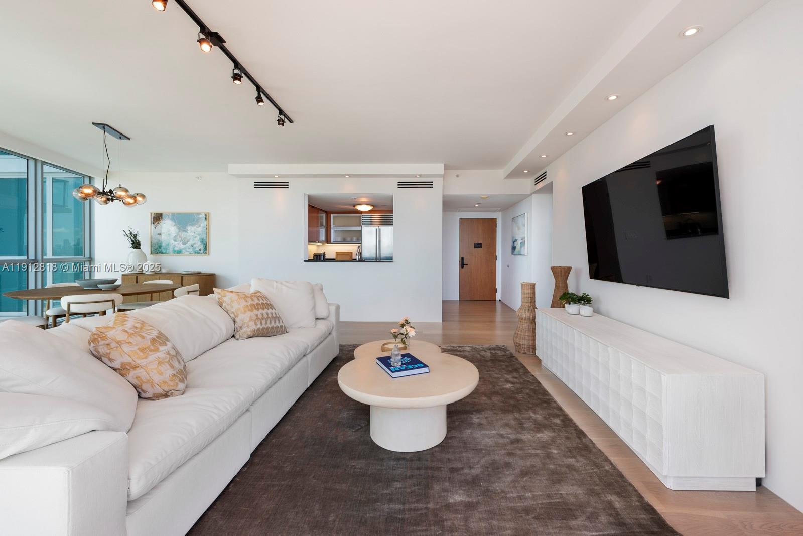 A modern living room features a white sofa, a coffee table, and a wall-mounted television — 101 20th St # 3006, Miami Beach FL 33139, MIAMI BEACH, FL