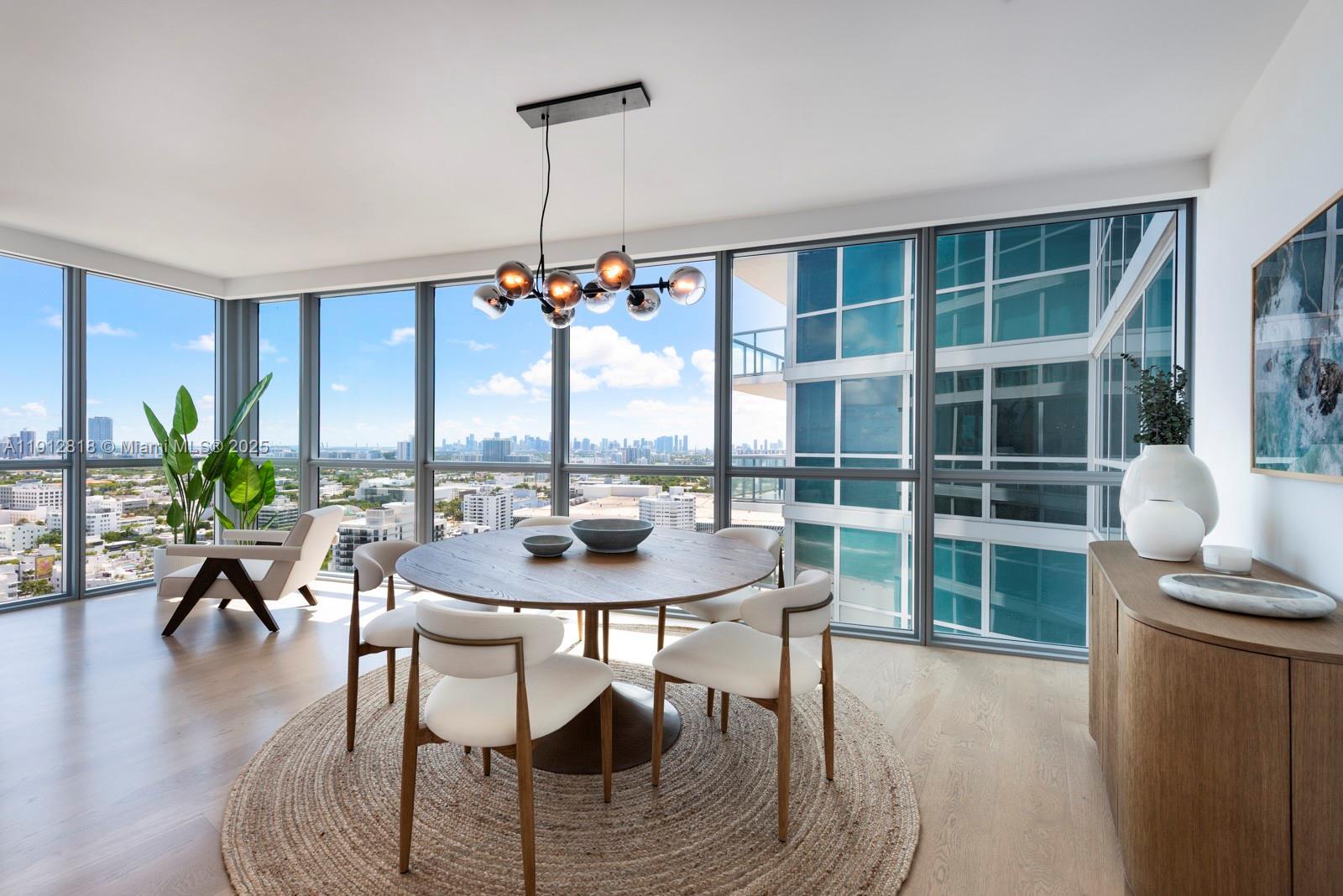 A dining area features a round wooden table, white chairs, and floor-to-ceiling windows with views — 101 20th St # 3006, Miami Beach FL 33139, MIAMI BEACH, FL