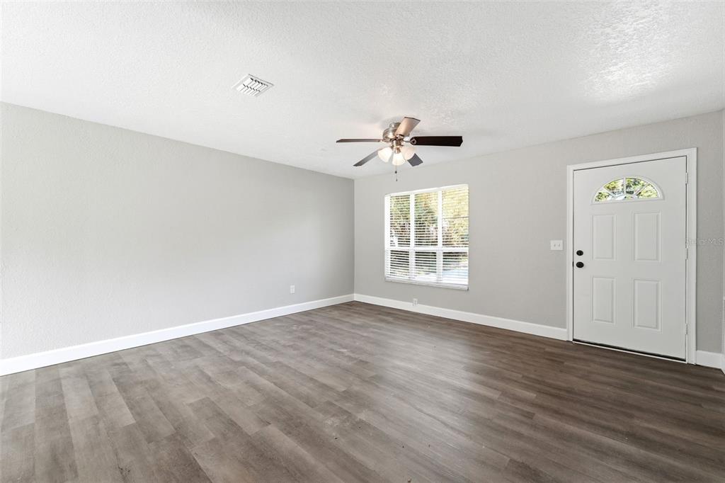 An empty room with light gray walls, wood-look flooring, a ceiling fan, and a front door — 451 S BLUE LAKE AVENUE, DELAND, FL