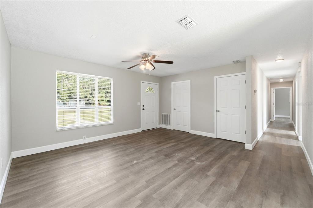 A living room features gray wood-look flooring, white walls, a ceiling fan, and three doors — 451 S BLUE LAKE AVENUE, DELAND, FL