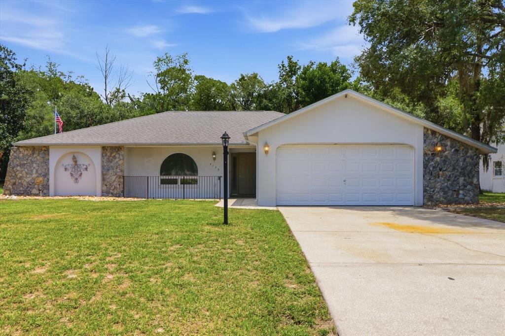 A single-story house with a white garage, stone accents, and a front lawn — 4179 S WINDING OAKS DRIVE, HOMOSASSA, FL