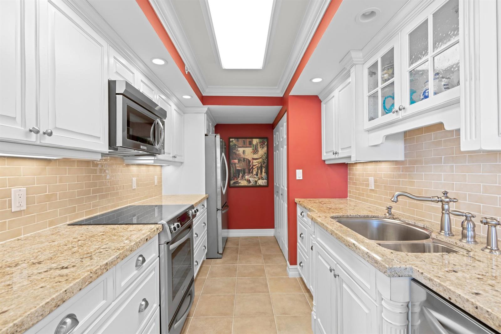 A galley kitchen features white cabinets, granite countertops, a beige tile backsplash, and red walls — 3000 N Ocean Drive # C, Singer Island FL 33404, SINGER ISLAND, FL