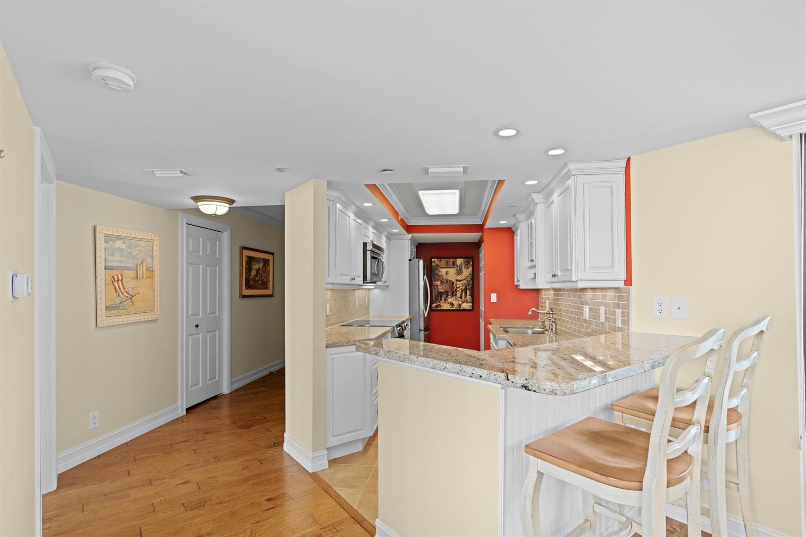 A kitchen with white cabinets, granite countertops, and a breakfast bar with two wooden stools — 3000 N Ocean Drive # C, Singer Island FL 33404, SINGER ISLAND, FL