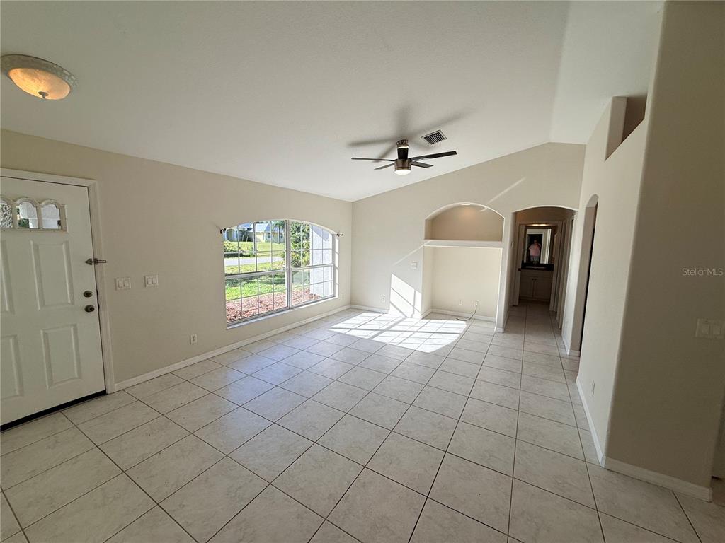 A living room with light-colored tile flooring, a vaulted ceiling, and a large arched window — 4185 AMARI ROAD, NORTH PORT, FL