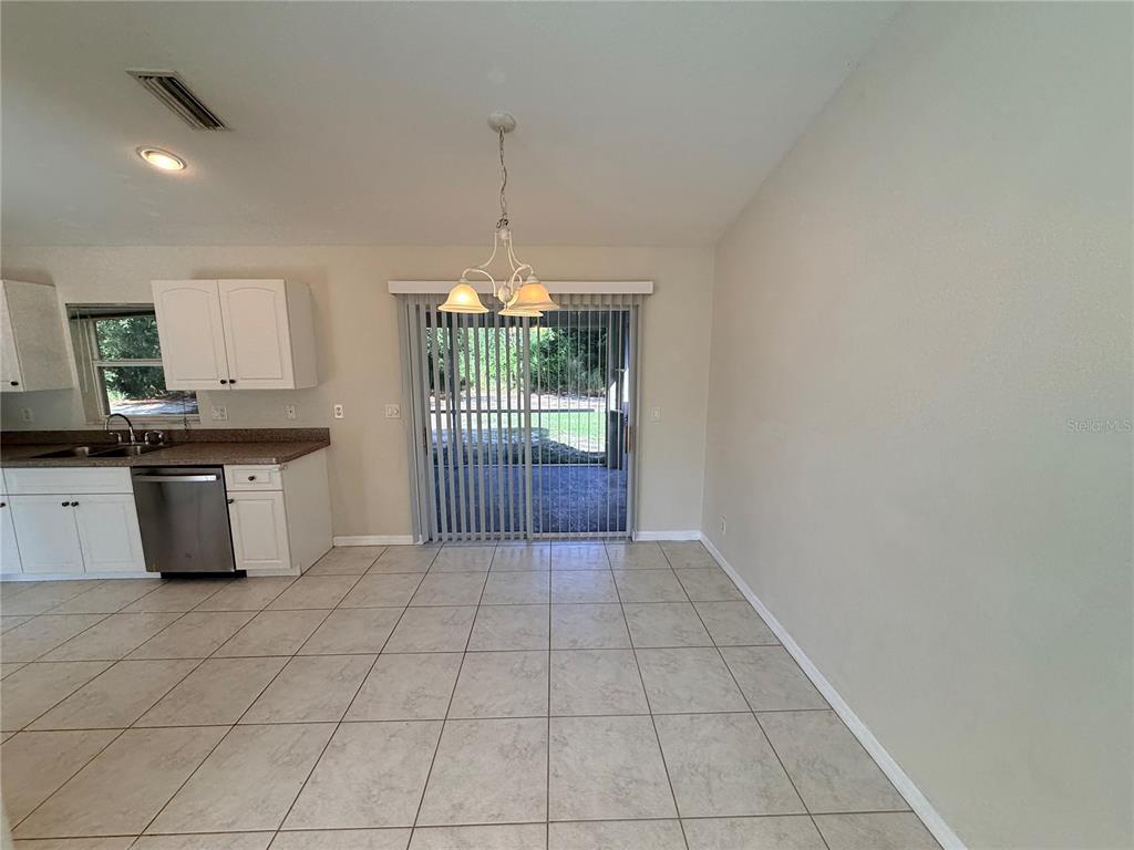 A kitchen with white cabinets and tile flooring opens to a dining area with sliding doors — 4185 AMARI ROAD, NORTH PORT, FL