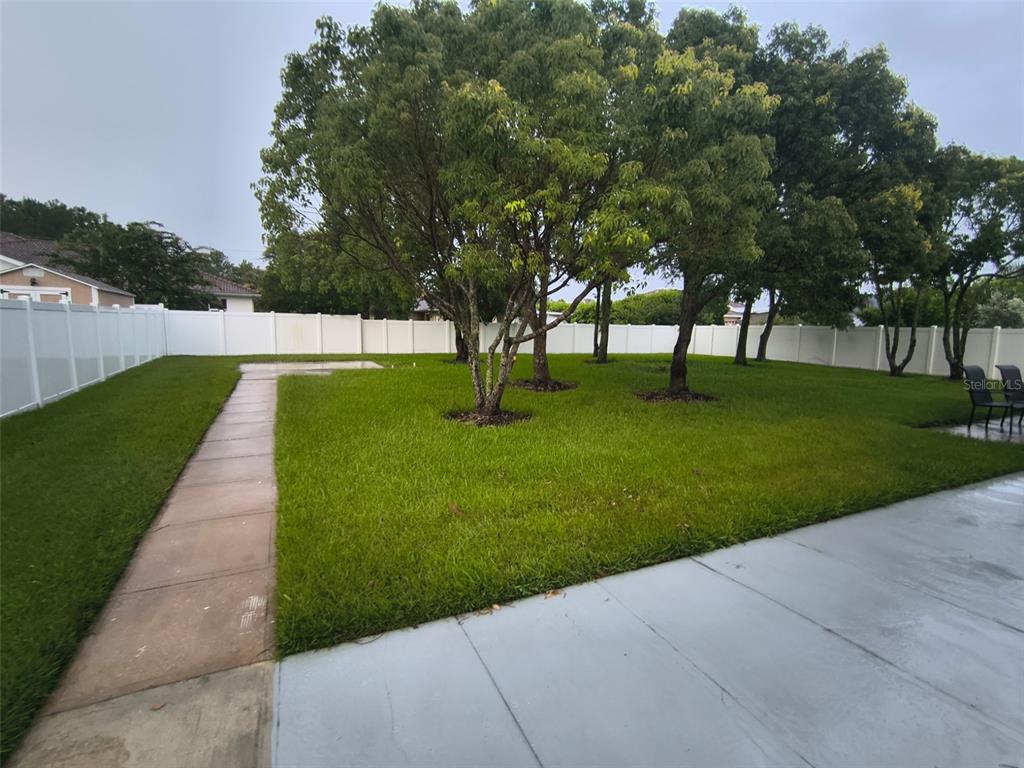 A fenced backyard features a concrete patio, a walkway, and several mature trees — 24 FELWOOD LANE, PALM COAST, FL