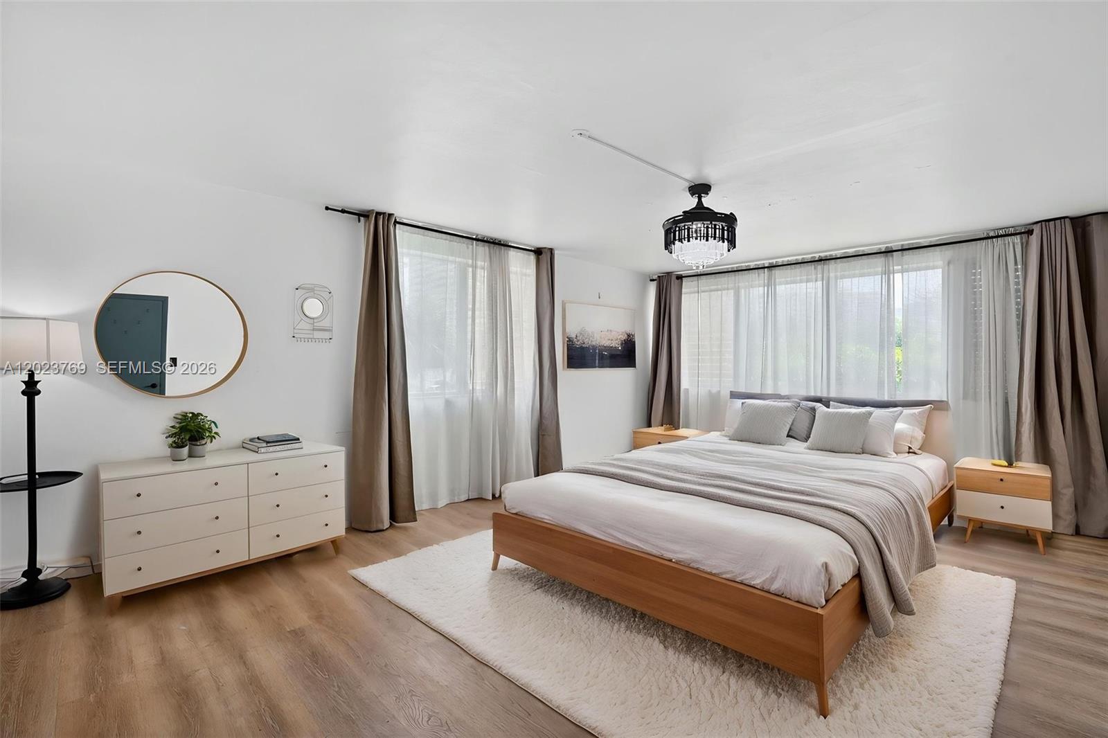 A bedroom features a wooden bed frame, white dresser, round mirror, and a chandelier — 10240 Collins Ave # 207, Bal Harbour FL 33154, BAL HARBOUR, FL