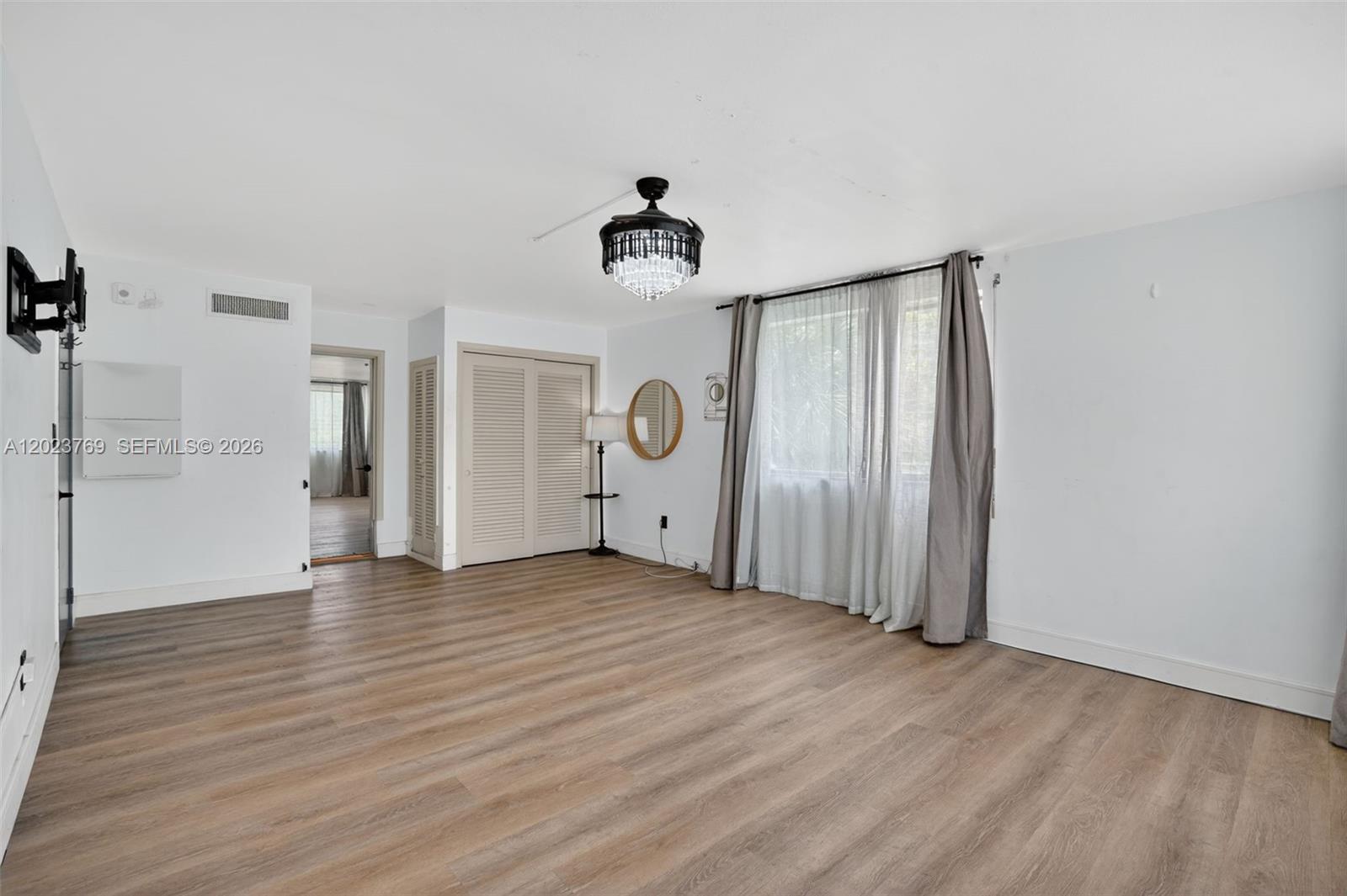 An empty room features light wood-look flooring, white walls, a crystal chandelier, and window curtains — 10240 Collins Ave # 207, Bal Harbour FL 33154, BAL HARBOUR, FL