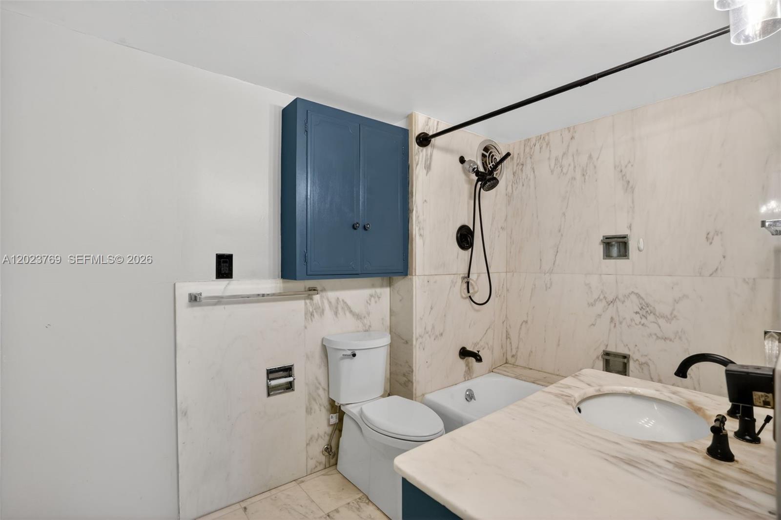 A bathroom features a marble-tiled tub surround, a blue cabinet, and a marble vanity top — 10240 Collins Ave # 207, Bal Harbour FL 33154, BAL HARBOUR, FL