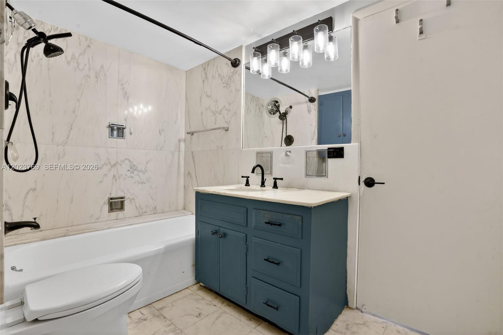 A bathroom features a blue vanity, marble-look wall tiles, and a shower-tub combination — 10240 Collins Ave # 207, Bal Harbour FL 33154, BAL HARBOUR, FL