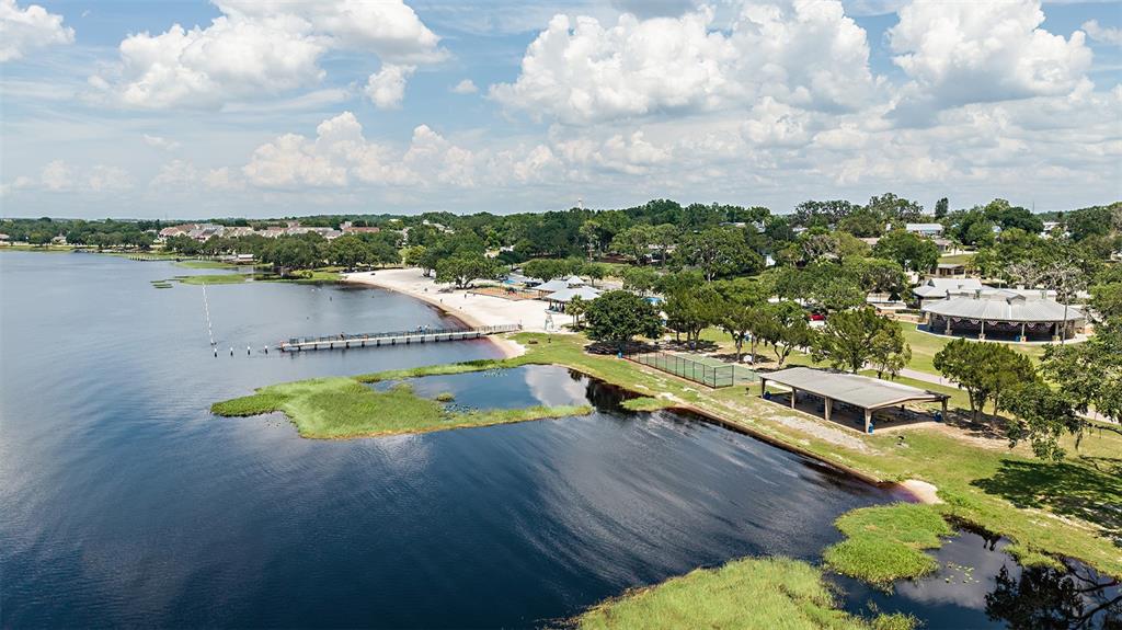 An aerial view of a lakefront park featuring a pier, sandy beach, and picnic pavilions — 229 STREAMWATER WAY, GROVELAND, FL