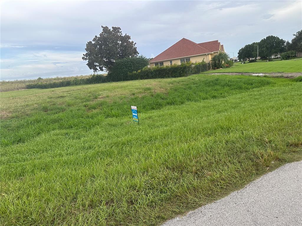 A grassy vacant lot with a real estate sign stands in front of a house — 529 SUNSET POINTE DRIVE, LAKE PLACID, FL