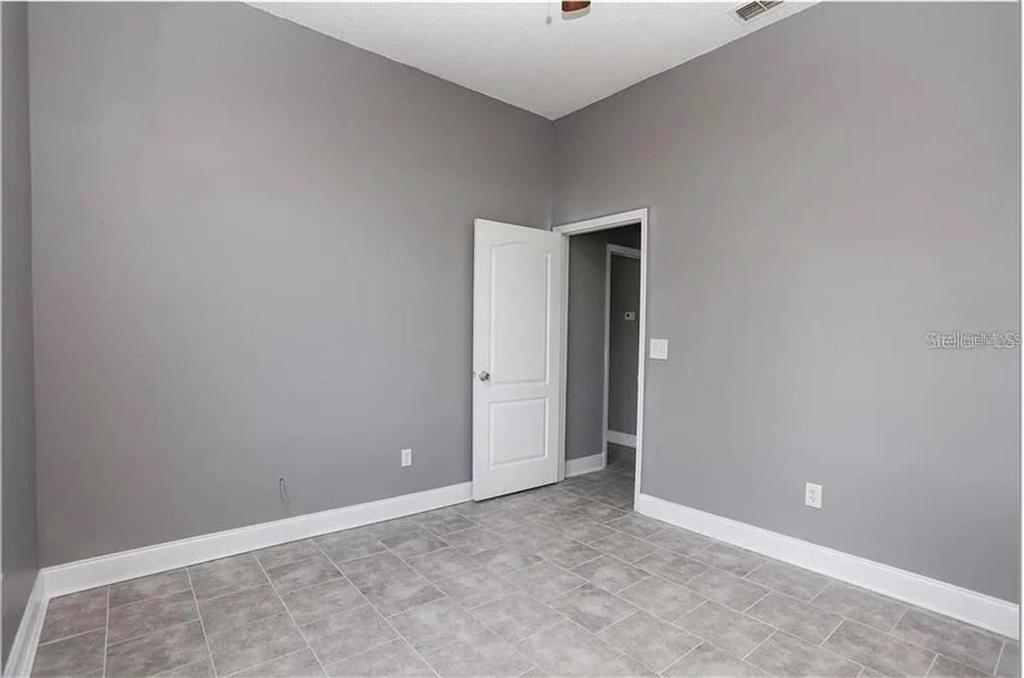 An empty room with gray walls, white trim, and gray tiled flooring — 12834 WOODBURY GLEN DRIVE, ORLANDO, FL