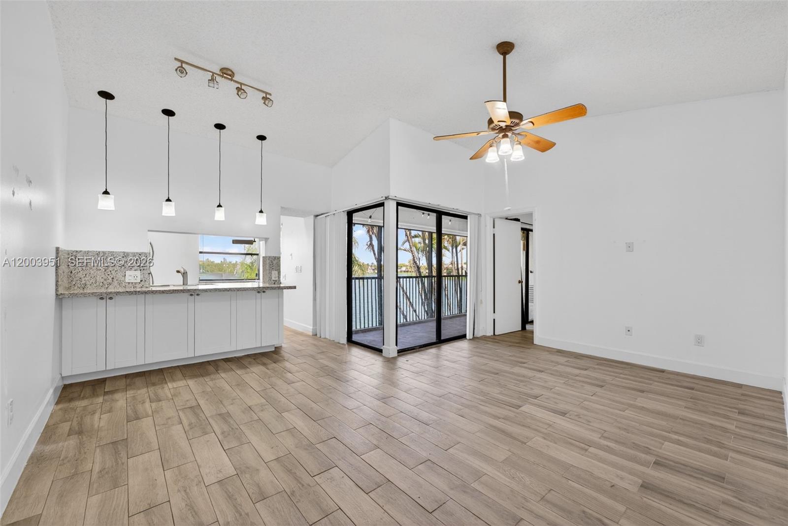 This living area features white walls, wood-look tile flooring, a kitchen counter, and a balcony — 889 Hamilton Dr # 889D, Homestead FL 33034, HOMESTEAD, FL