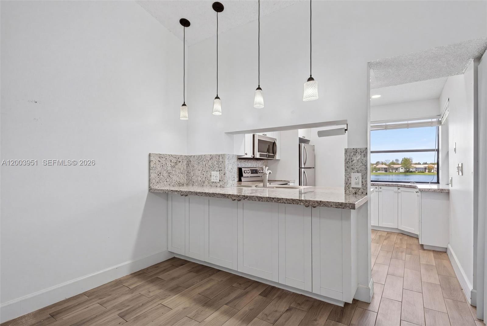 A kitchen features white cabinets, granite countertops, four pendant lights, and a view of water — 889 Hamilton Dr # 889D, Homestead FL 33034, HOMESTEAD, FL