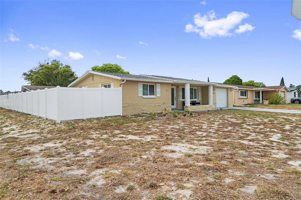 A single-story tan house with a white fence and a sparse, sandy front yard — 3619 QUINTEN DRIVE, NEW PORT RICHEY, FL