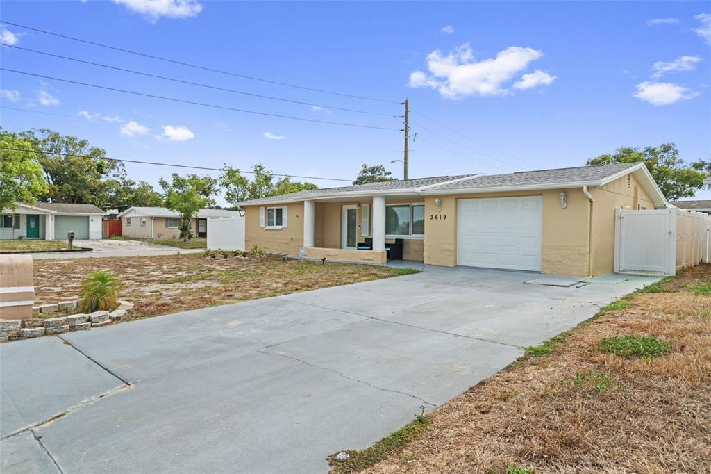 A single-story house with a tan exterior, a white garage door, and a concrete driveway — 3619 QUINTEN DRIVE, NEW PORT RICHEY, FL