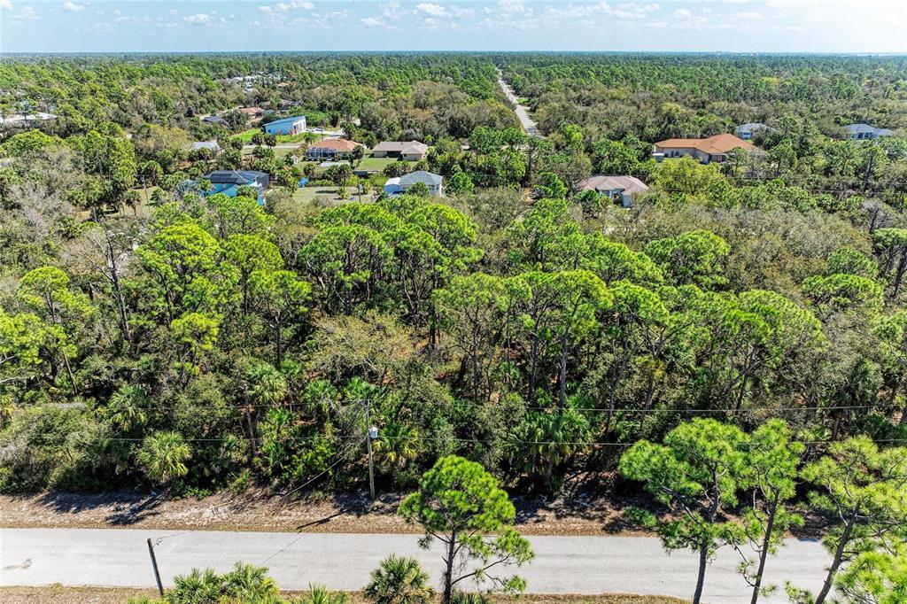 An aerial view shows a wooded residential lot next to a paved road and houses — 3059 COMO STREET, PORT CHARLOTTE, FL