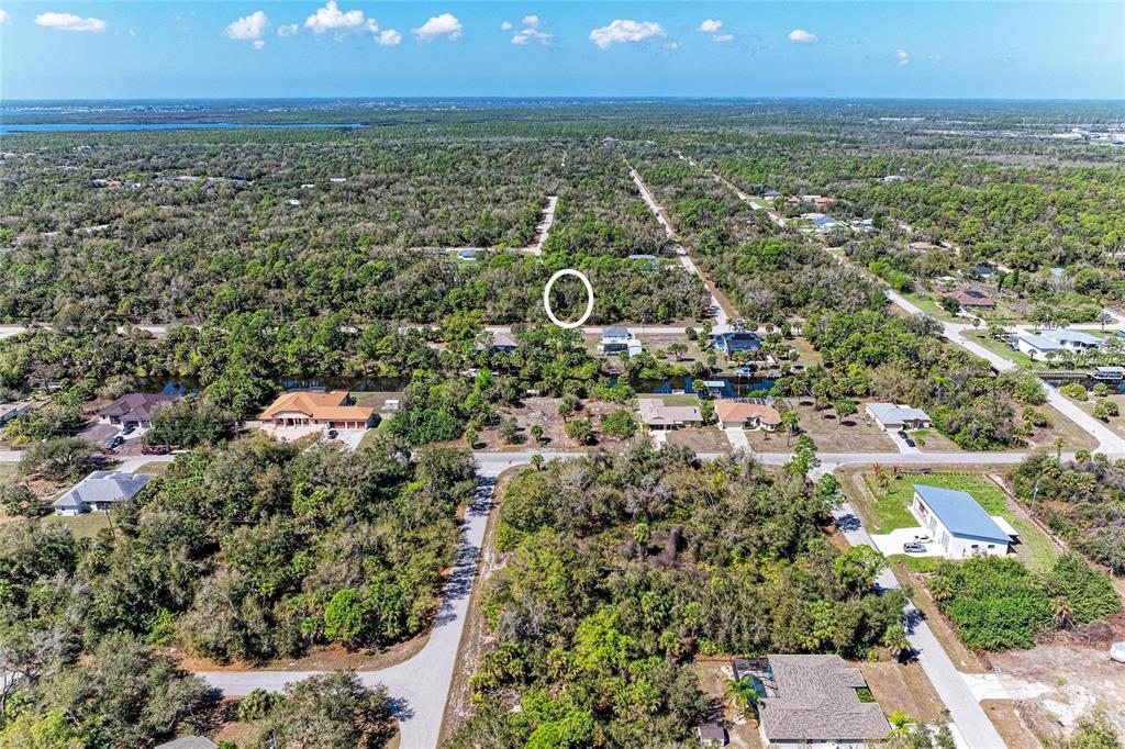 An aerial view shows a residential neighborhood with houses, wooded lots, and a canal — 3059 COMO STREET, PORT CHARLOTTE, FL