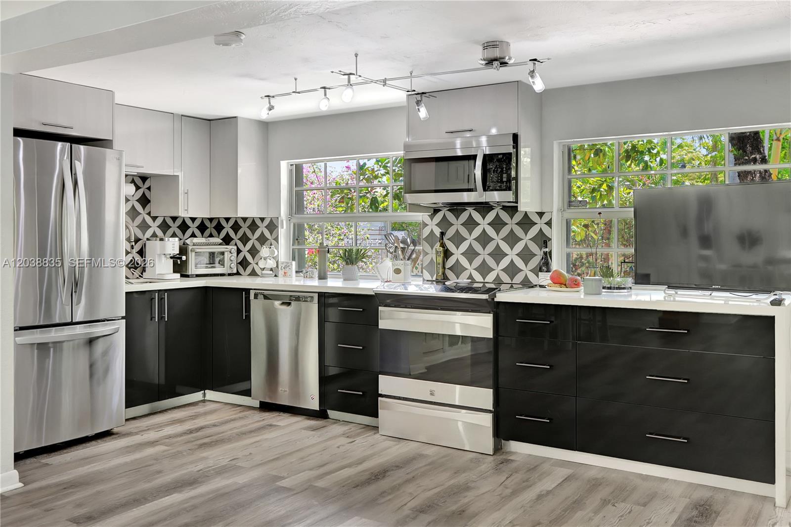 A modern kitchen features black and white cabinetry, stainless steel appliances, and a geometric backsplash — 3375 SW 29th Ter, Miami FL 33133, MIAMI, FL